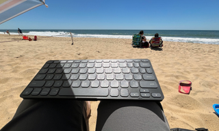 A Logitech Keys-To-Go 2 keyboard resting on a person's lap while on the person is on the beach.