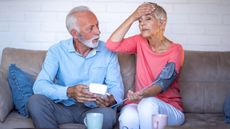 An older man looks concerned as he helps his stressed wife take her blood pressure.