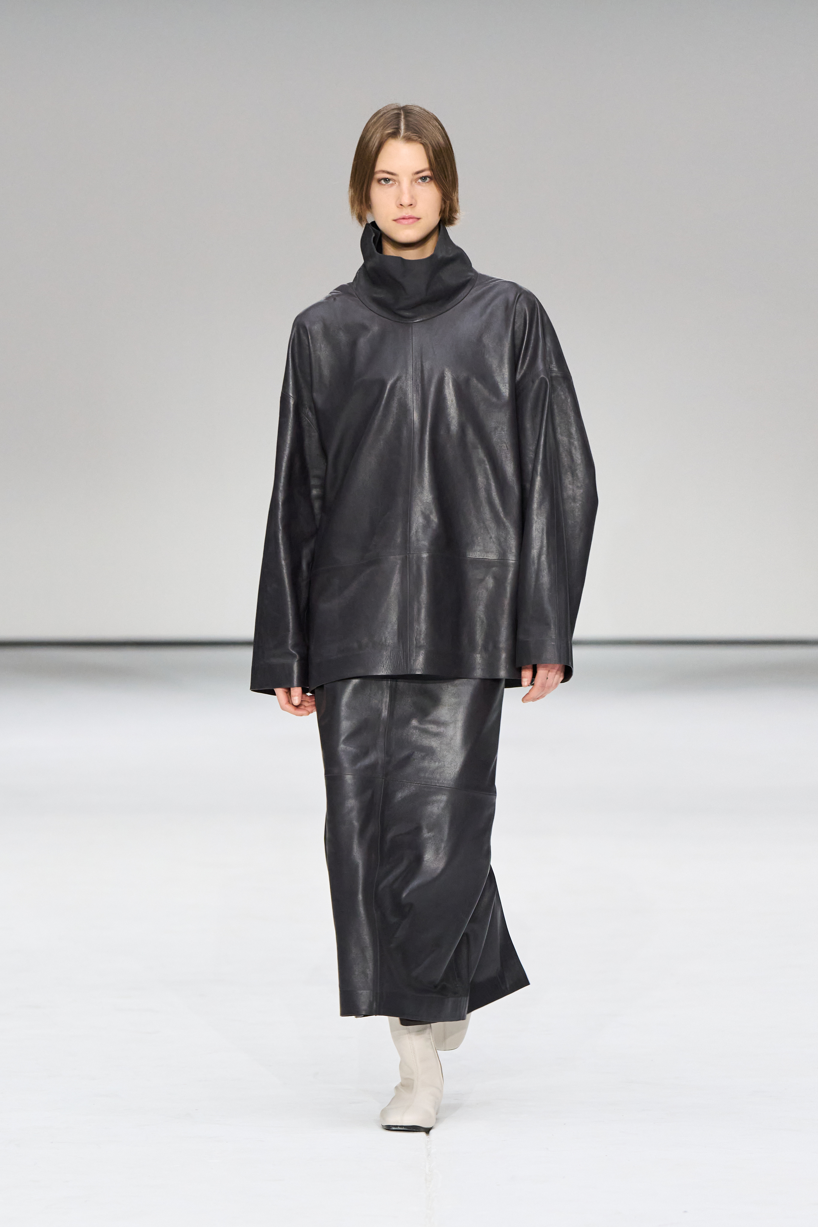 A woman wears a leather funnel-neck top and leather skirt.