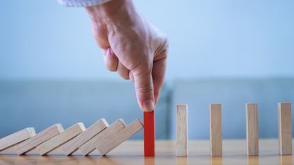 A man places a red, protective block between blocks that are tipping over and blocks that are standing upright.