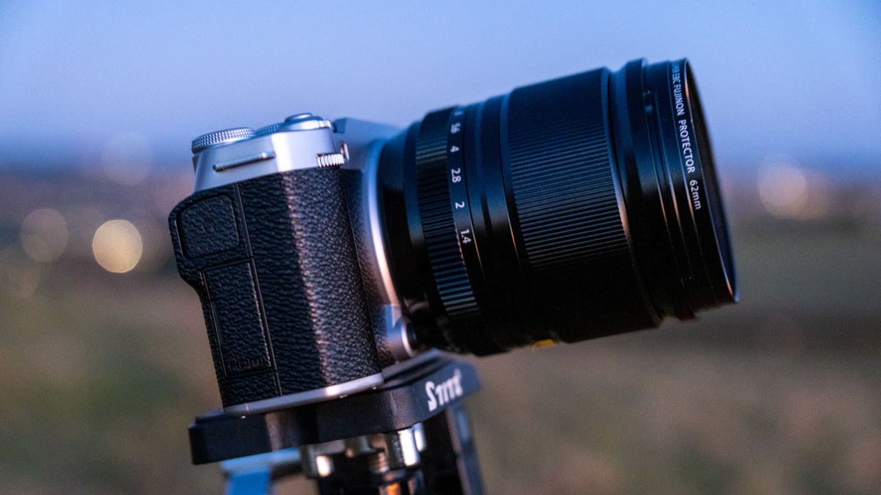 The Fujifilm X-M5 with XF 18mm f/1.4 lens on a tripod head angled up, with a field in the background.