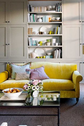 Neutral living room with yellow velvet sofa and bespoke shelves with intential items on displays to show how to declutter a living room in style