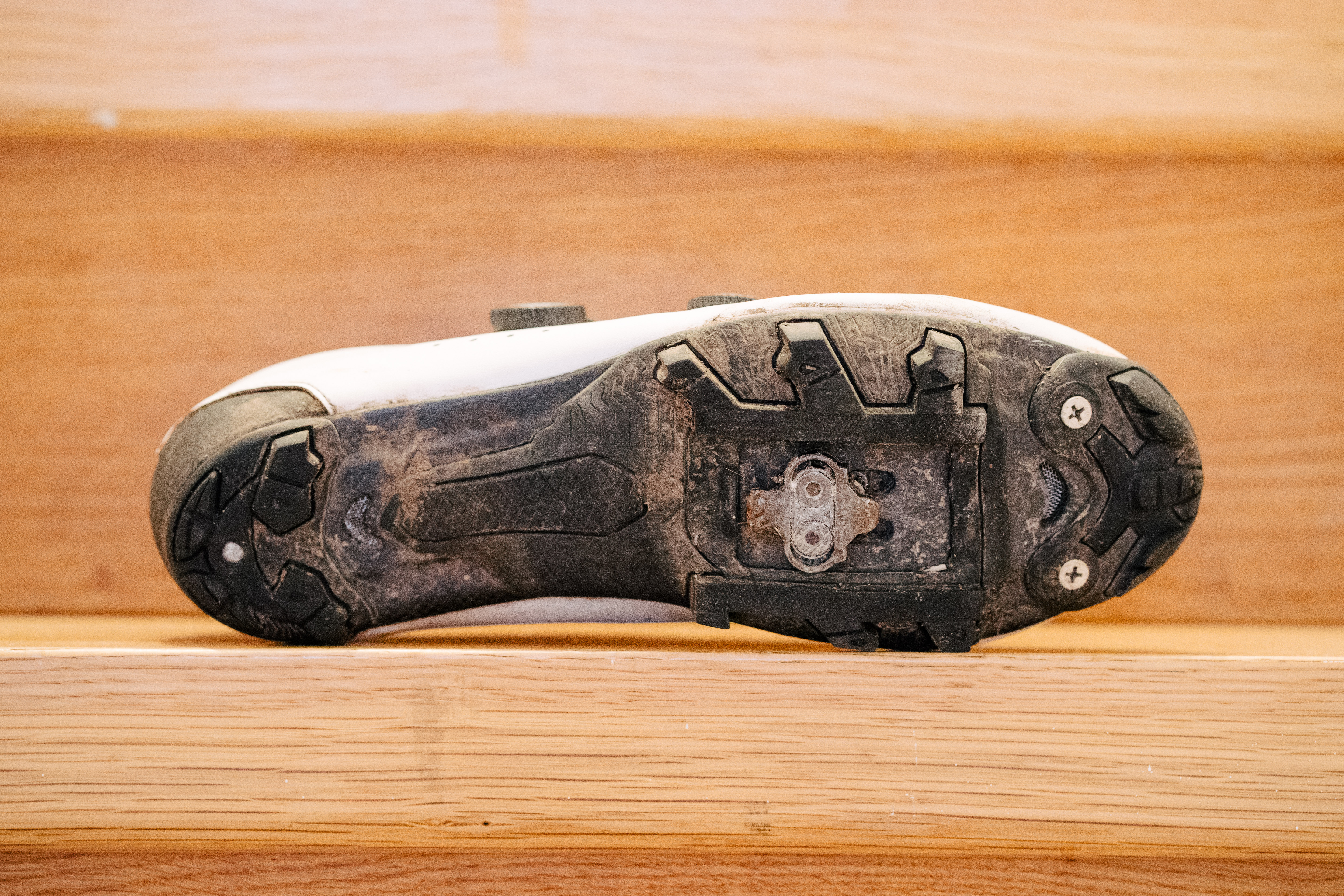 A white gravel bike shoe on wooden stairs
