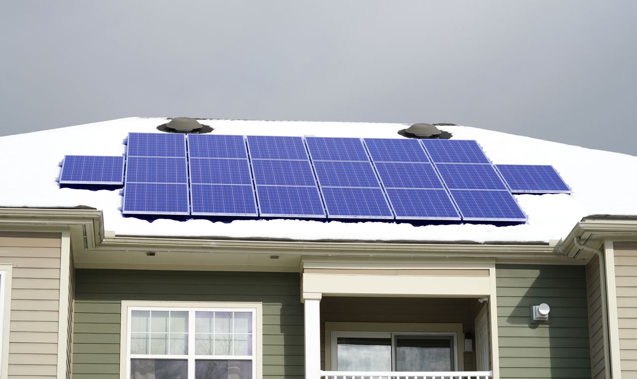 solar panels on a roof amidst snow with a gray sky above