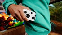 A person in a teal hoodie holds a white Xbox controller in front of a TV showing a colorful video game, creating a relaxed gaming mood.
