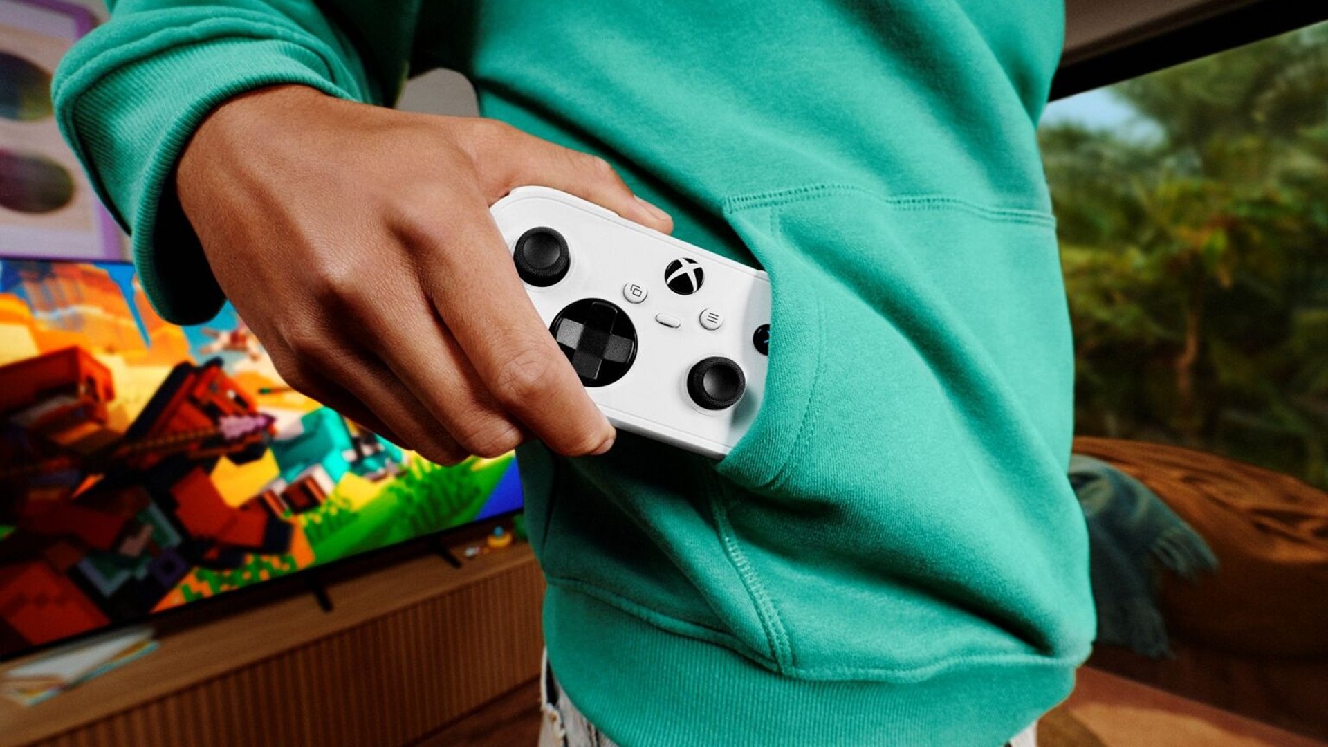 A person in a teal hoodie holds a white Xbox controller in front of a TV showing a colorful video game, creating a relaxed gaming mood.