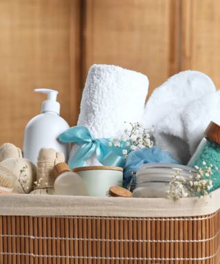 A wooden basket containing towels, slippers, and toiletries against a wood wall.