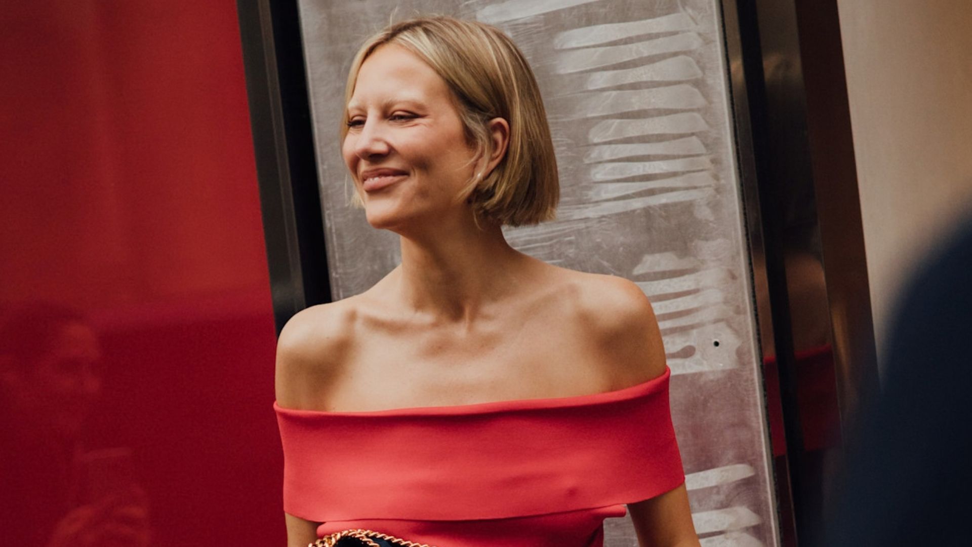Paris Fashion Week Attendee wears a red top with blue jeans and heels, outside of a runway show.