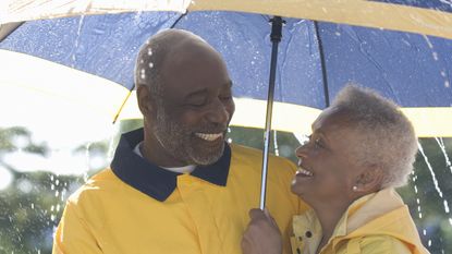 An older couple smile at each other while holding an umbrella overhead.