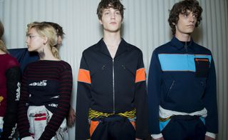 Three models wearing clothing by Prada in various colours.