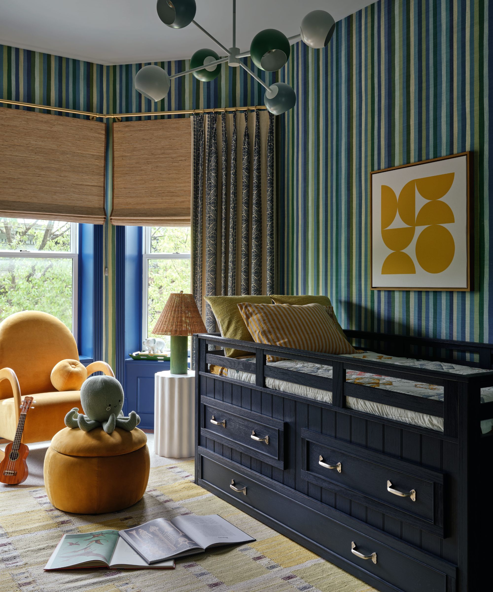 a blue and green striped kids bedroom with a bay window, built in navy storage bed, orange armchair in the window and a small stool with an octopus toy