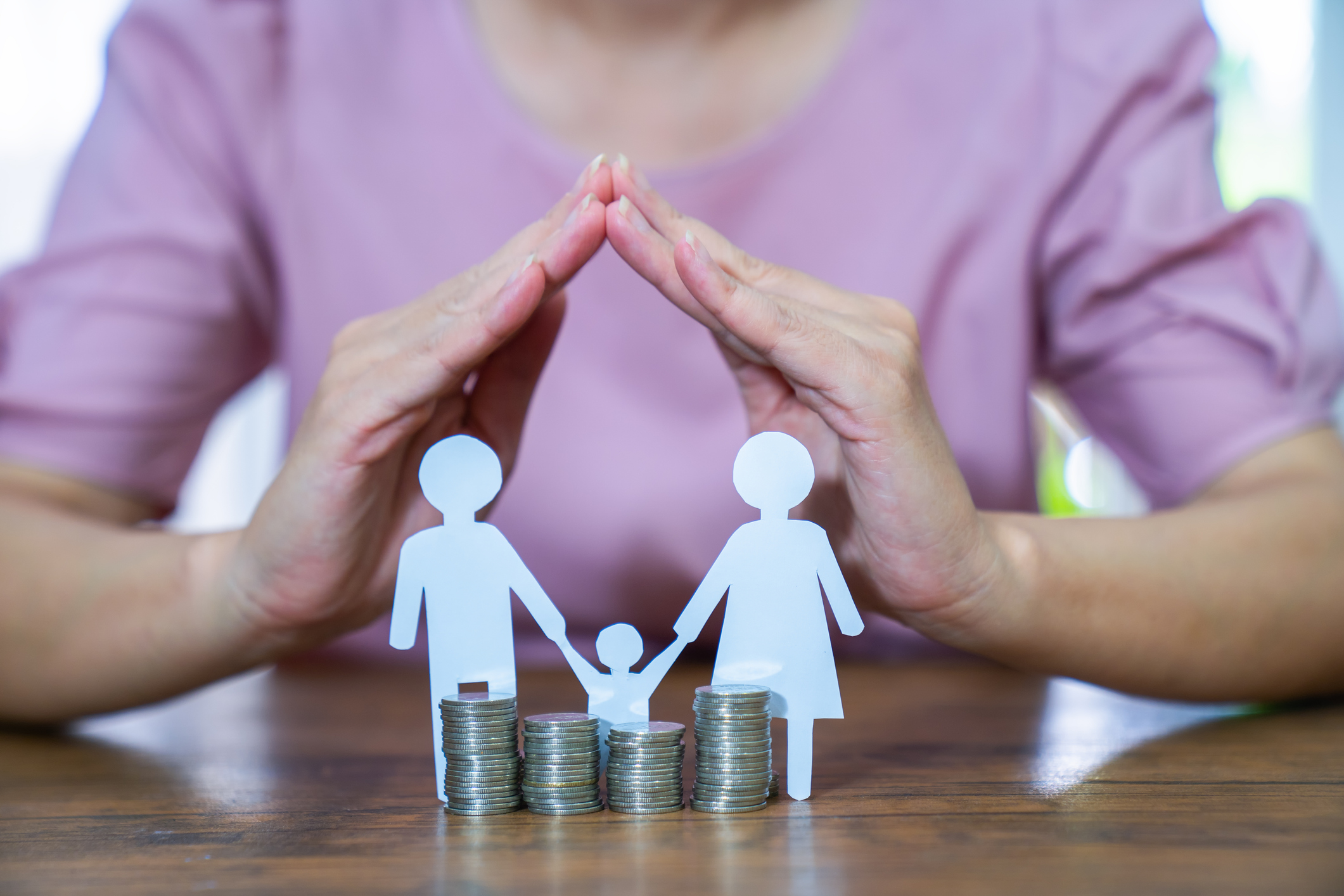 A picture of a cutout family around coins with hands protecting them, indicating how insurance financially protects your loved ones