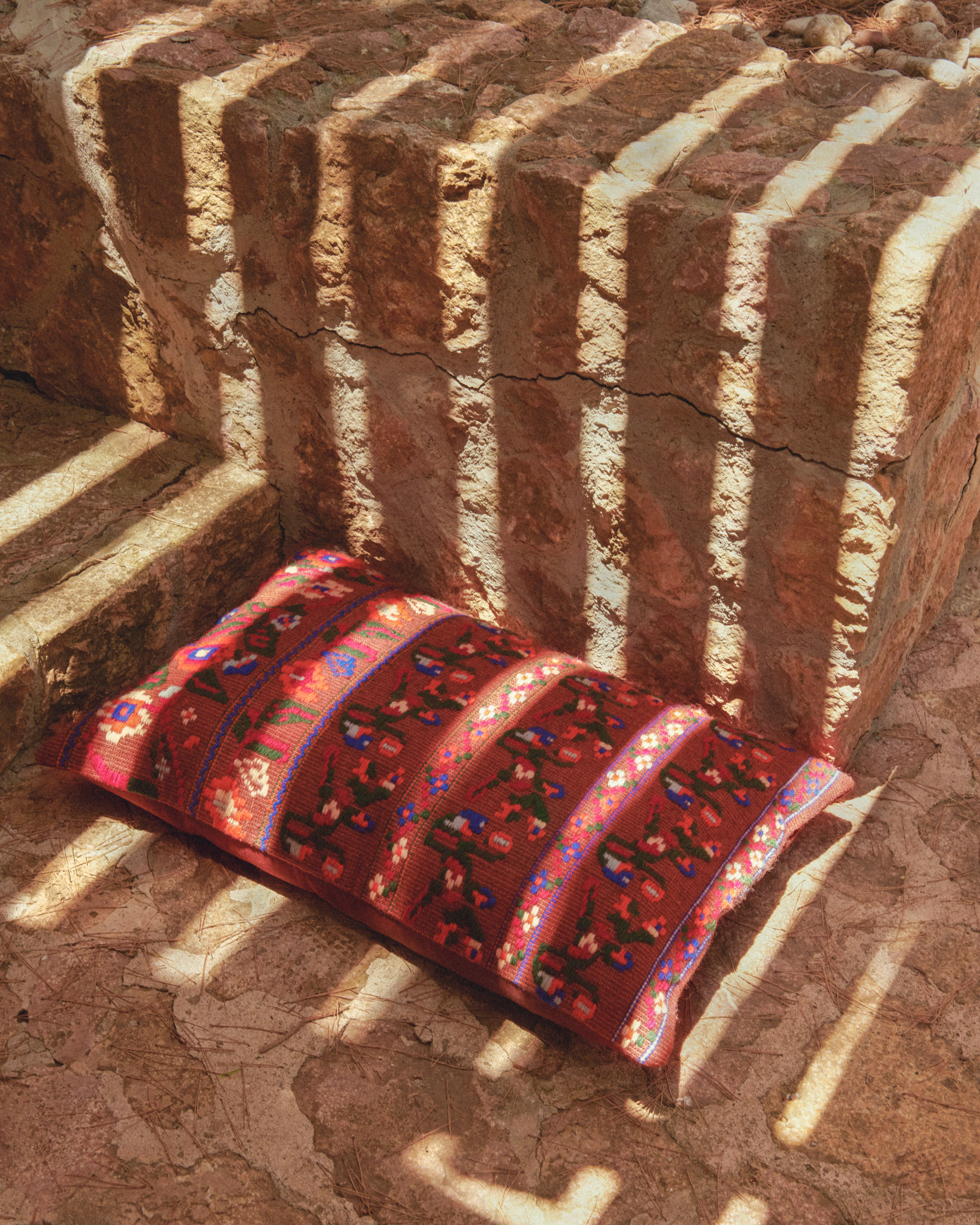 embroidered cushion on a sun dappled stone floor