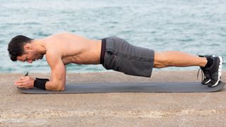 Man performing a forearm pillar bridge plank outdoors next to the water