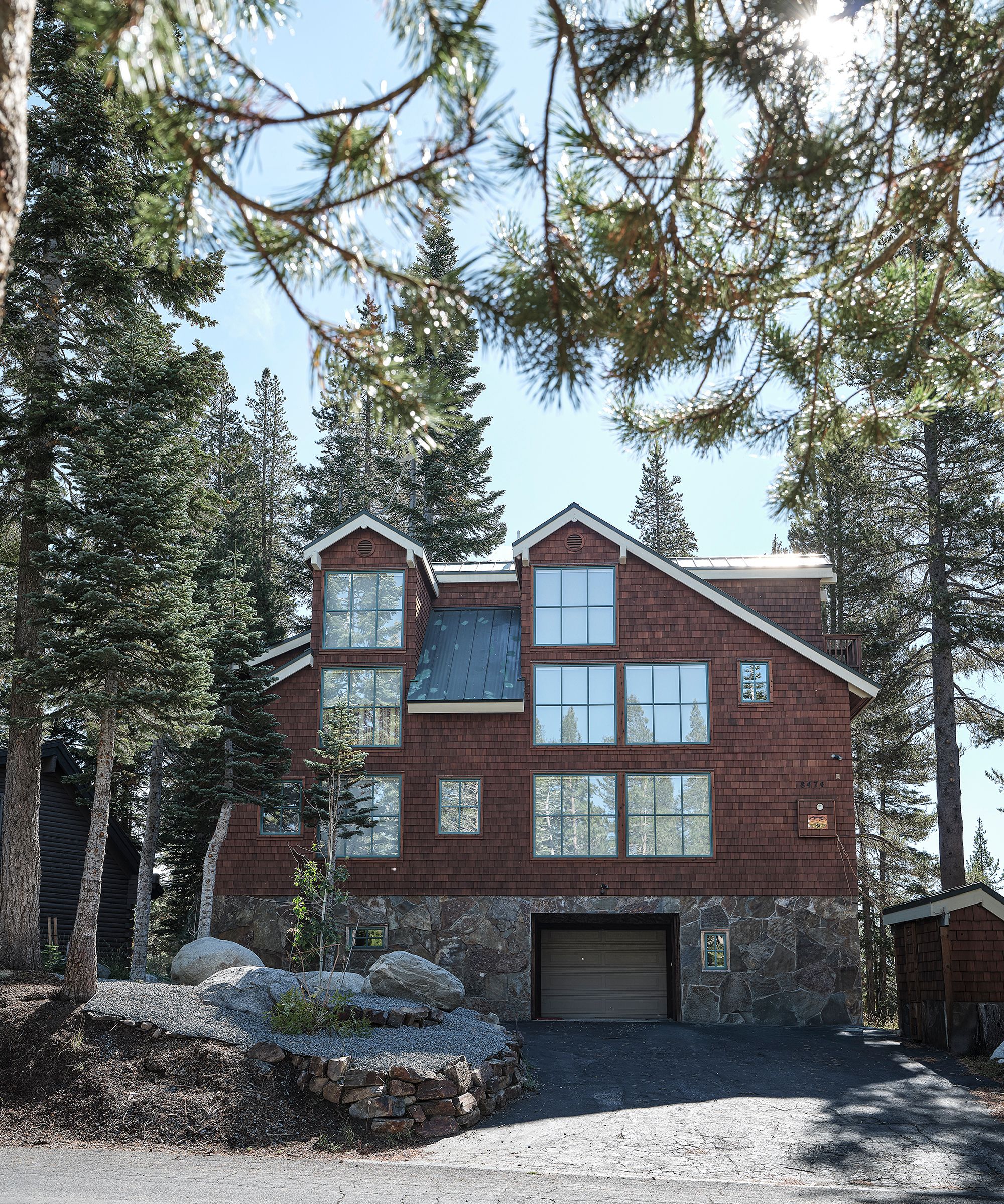 an exterior shot of a ski chalet surrounded by trees with a sloping driveway and traditional tile and stone facade