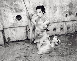 Japanese woman sitting on concrete prison floor, hands tied with rope