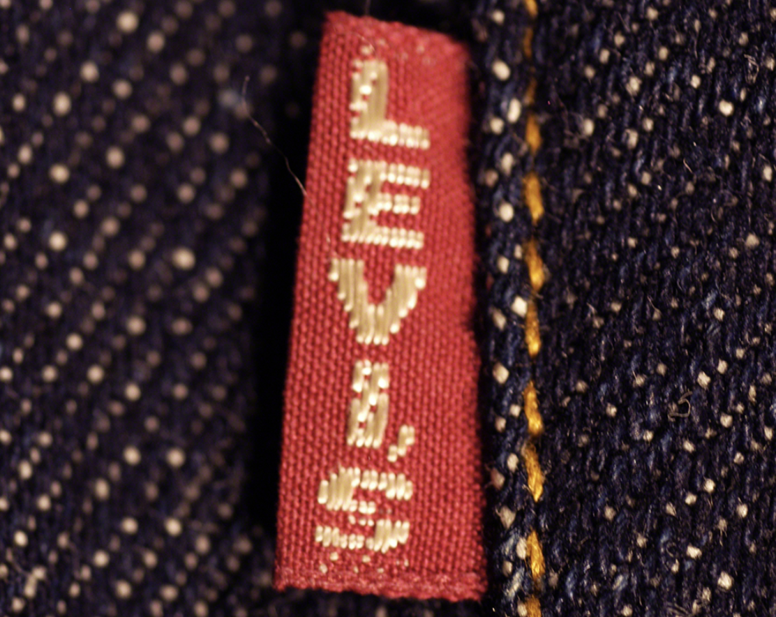 A close-up shot of a classic red Levi's brand tab with white embroidered lettering sewn into the seam of dark blue denim fabric.