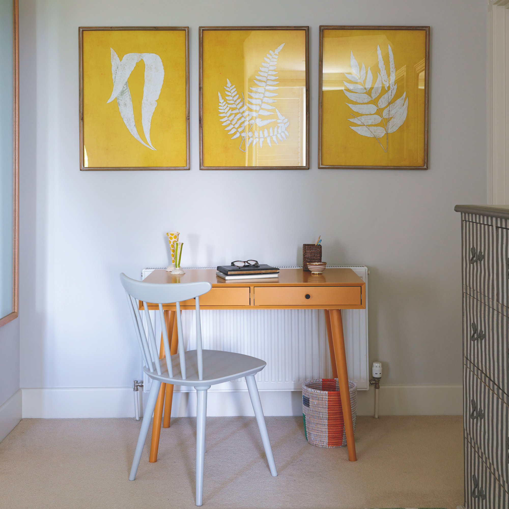 small wooden desk with painted wooden chair in front and three leaf-design prints on wall above