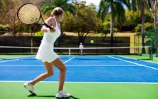 A woman with her blonde hair in a braid prepares to hit a tennis ball across the net at her playing partner who is an older man with white hair