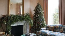 Christmas tree in living room next to blue floral couch. Garland on the mantelpiece
