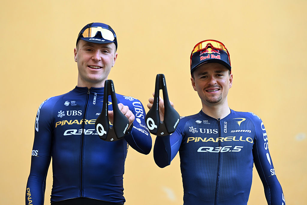Fred Wright and Tom Pidcock pose together holding team saddles and smiling