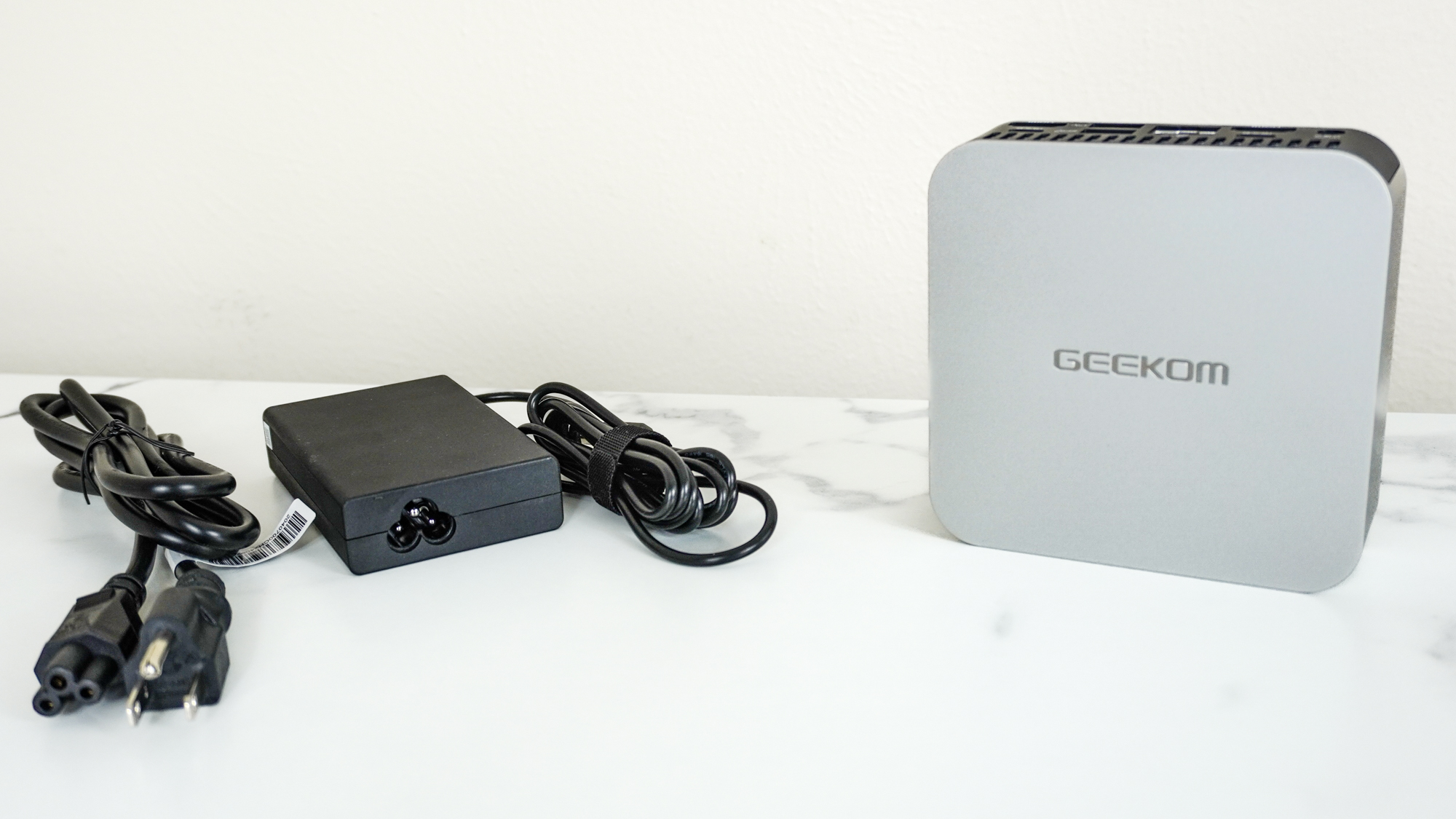 The Geekom A6 upright on a desk next to its external power brick