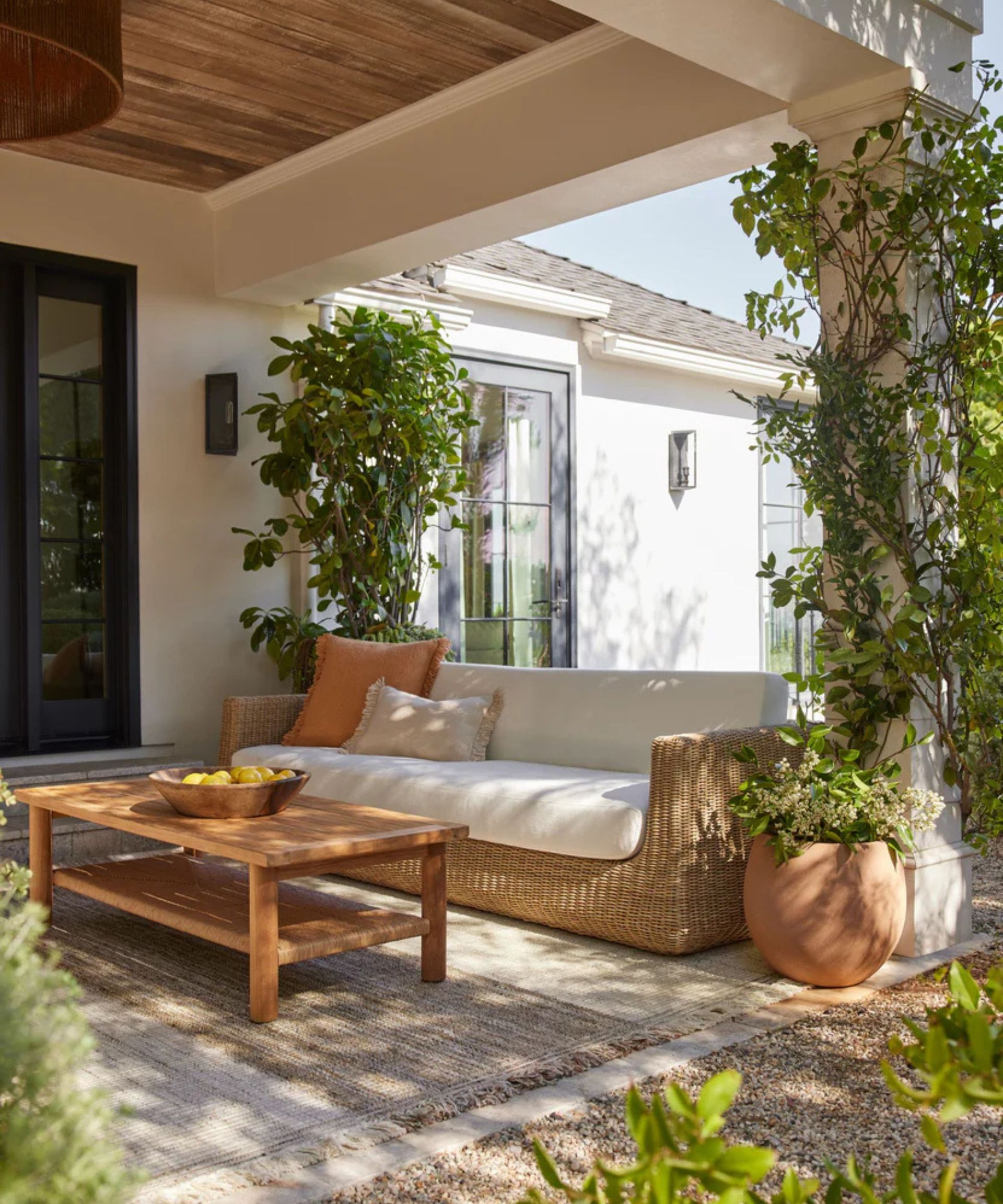 Aisha Indoor/Outdoor Sofa on a patio surrounded with plants against a house with white walls.