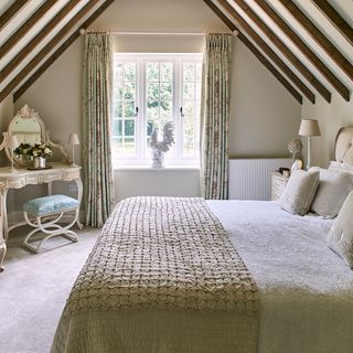 bedroom with sloped ceiling and beams cream colour wall and bed with embroidered cushions