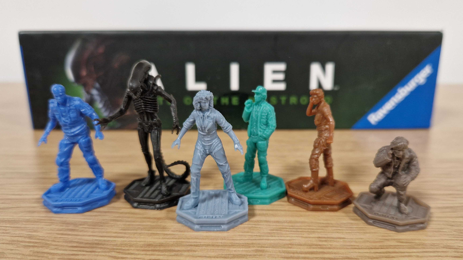 Miniatures from Alien: Fate of the Nostromo lined up in front of the box, all on a wooden surface
