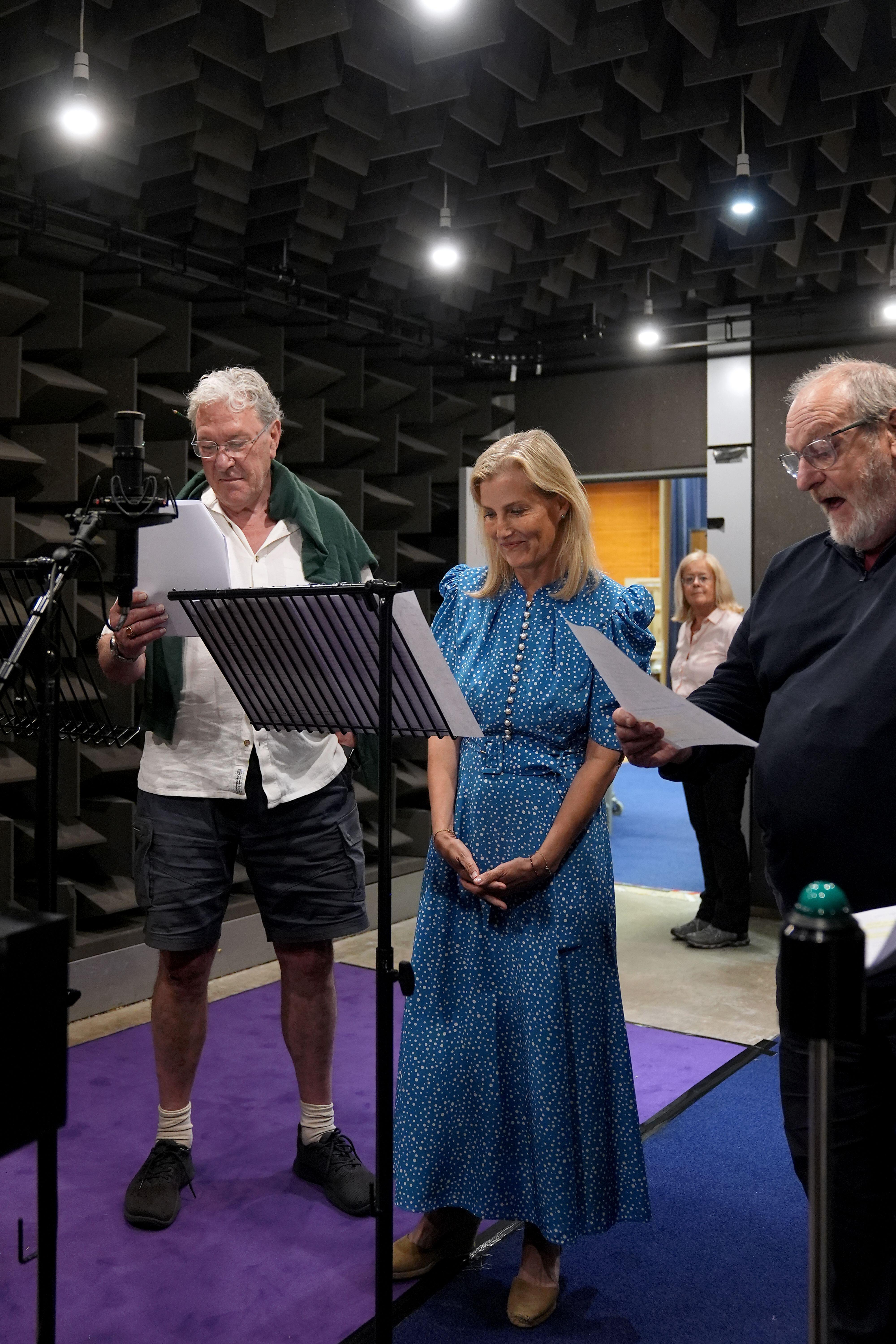 Duchess Sophie wearing a blue dress standing with two men in front of microphones