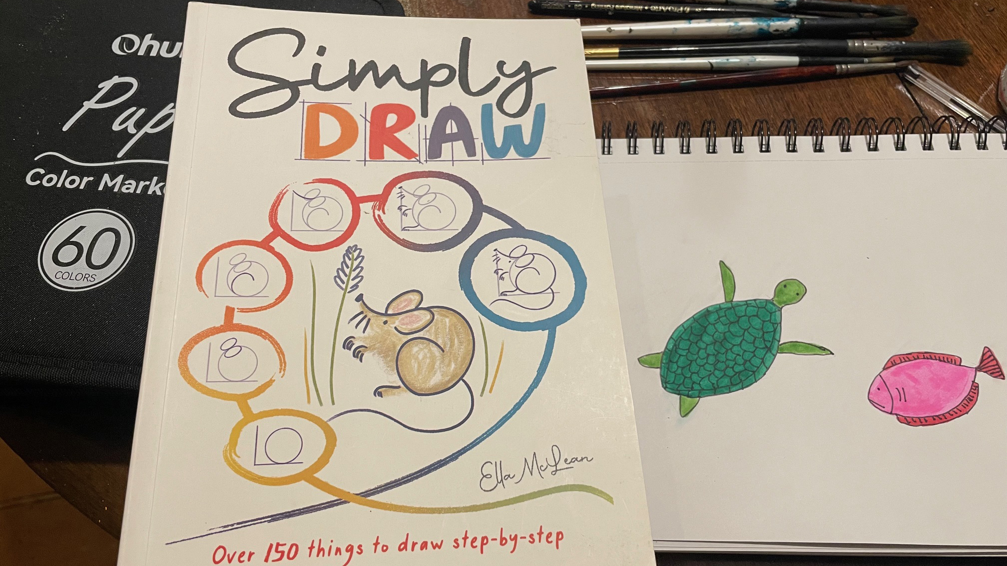 drawing of a turtle and a fish in felt tip pen next to a book with instructions on how to draw