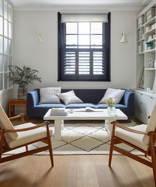 A pale living room color scheme with blue sofa and symmetrical mid-century modern wooden chairs.