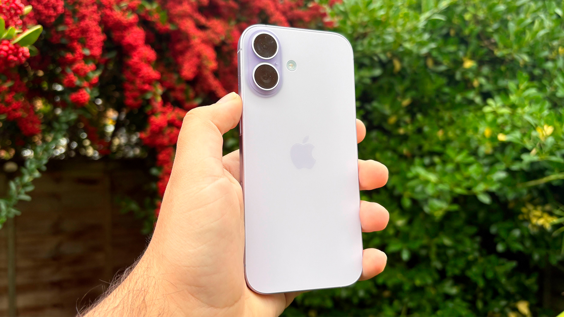 Apple iPhone 17 smartphone held in hand in front of bushes, showing rear of phone