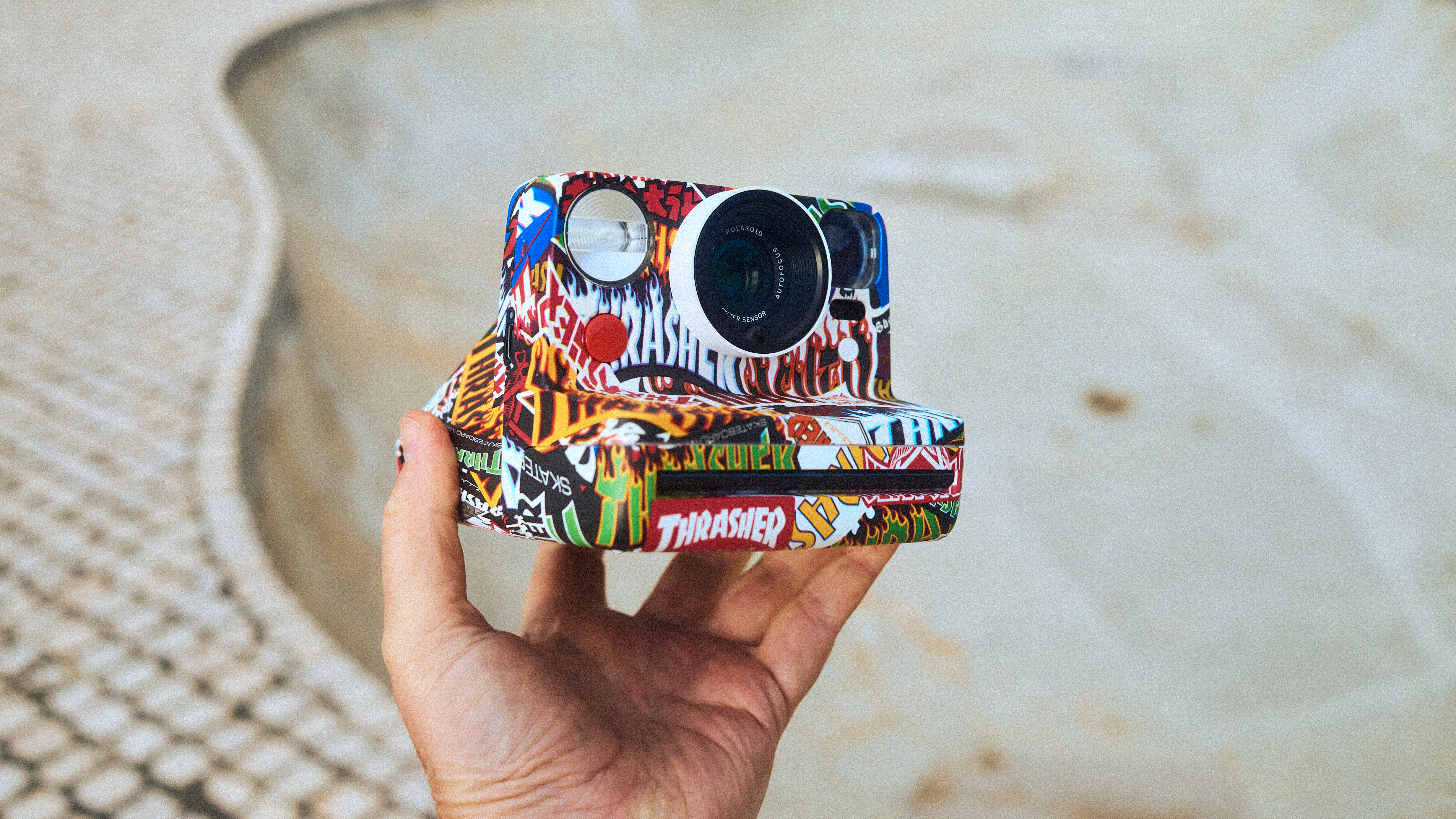 Polaroid Now Thrasher Edition being held up above with a skatepark in the background