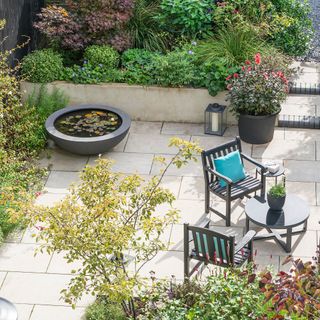 Patio area with pond, red dahlias in pot and black garden seating