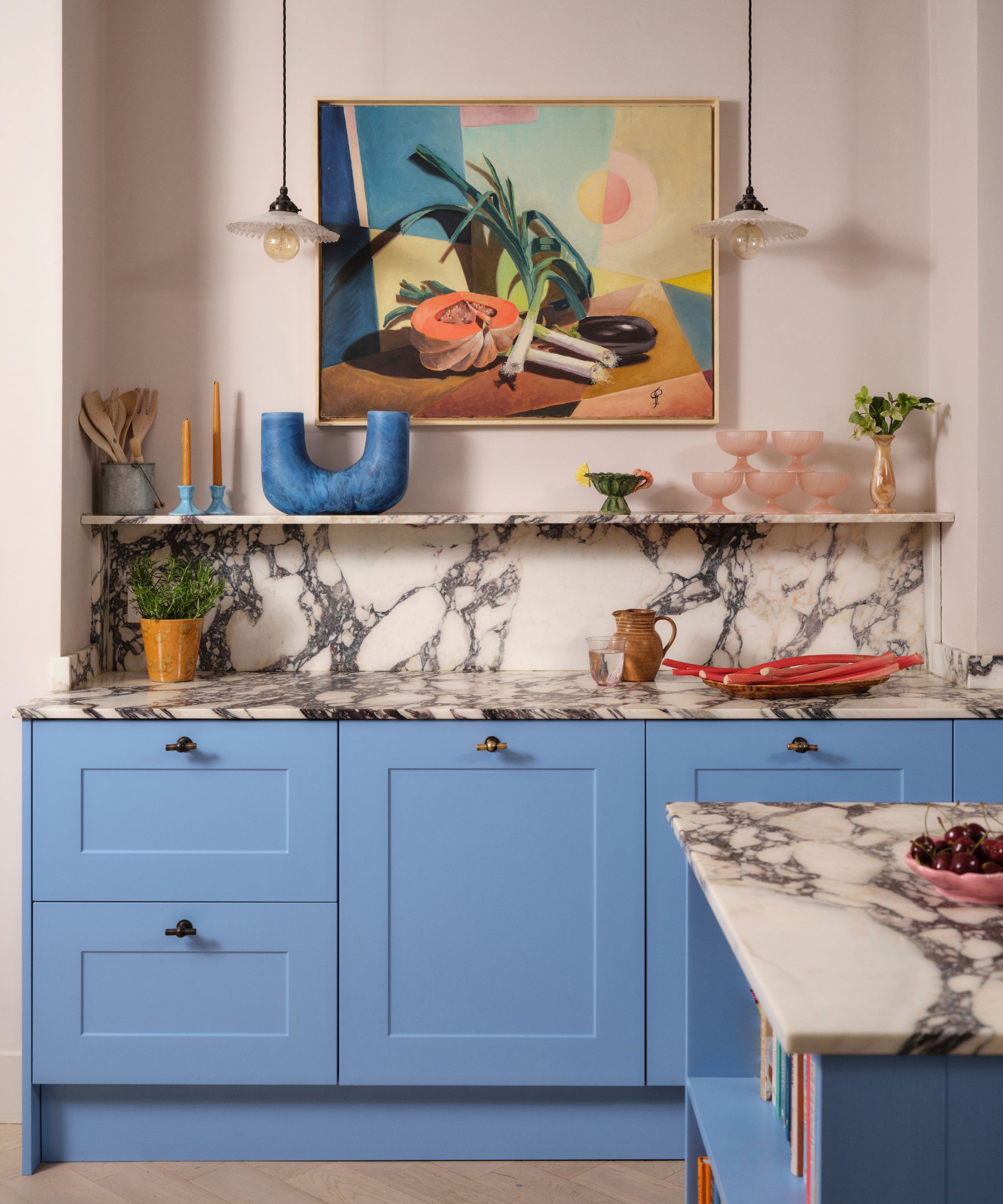 A kitchen with blue cabinets, marble countertops, and an island with a bookshelf at the end