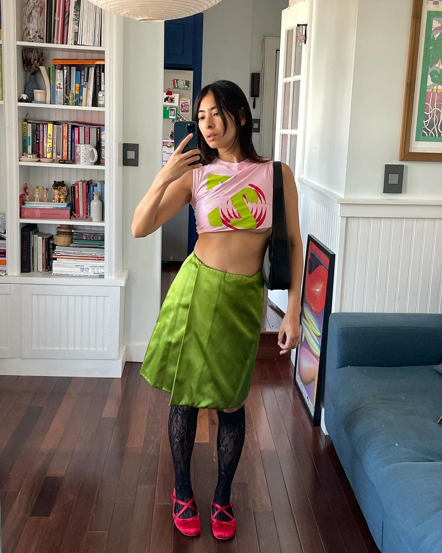 Fashion person Michelle Li wears black lace knee-high socks. She pairs them with a green skirt, a pink cropped tank and red ballet flats in a recent image from her Instagram.
