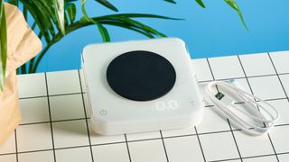 the acaia pearl s coffee scale with an LED screen, on/off, tare button with slip-proof feet and a premium white exterior plastic casing photographed against the tom's guide blue background