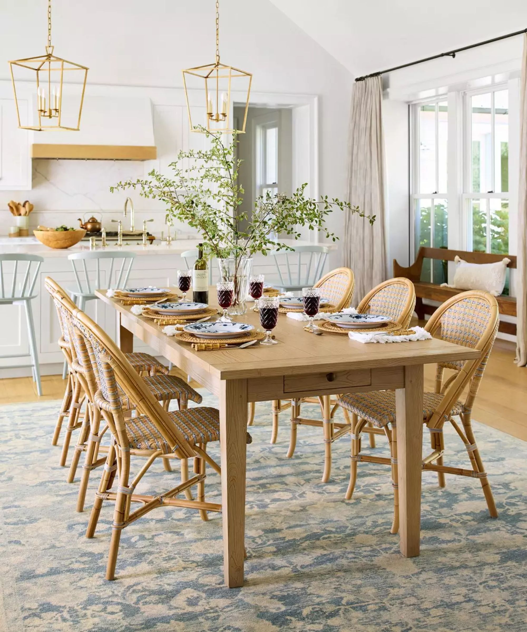 coastal kitchen diner with a white kitchen, large oak table and cane chairs laid for dinner with a large blue vintage style patterned rug