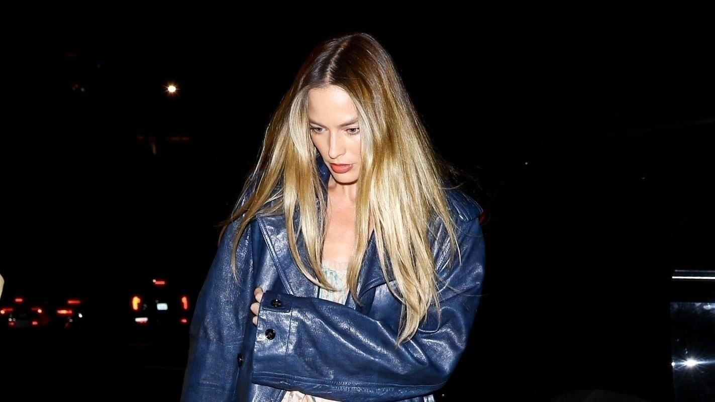 Margot Robbie wearing a navy leather coat, ruffled top, jeans, and satin ballet flats