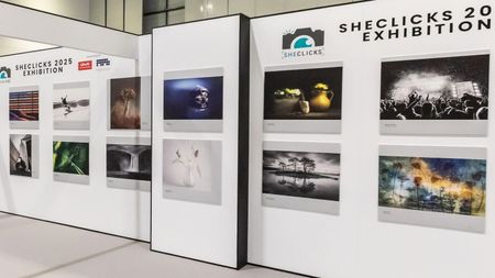 Wall display featuring diverse photographs at the SheClicks 2025 Exhibition, highlighting various artistic themes and styles