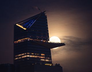 the moon behind the ridge of a tall building