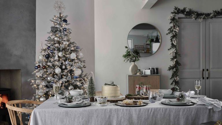 A Scandinavian-style dining room with linen tablecloth, wooden chair and large frost-effect artificial Christmas tree