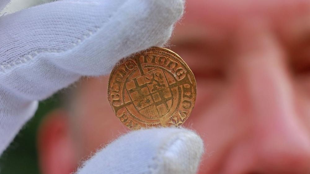 A person wearing white gloves holds a gold coin.