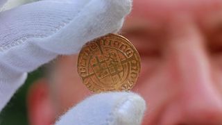 A person wearing white gloves holds a gold coin.