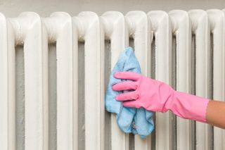Person wearing a pink rubber glove wiping down a traditional column radiator with a blue cloth