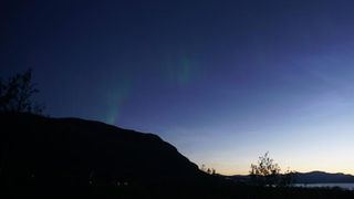 faint green auroras in top left of the image and thin wispy noctilucent clouds on the right. 