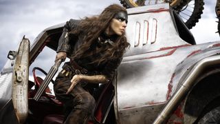 A menacing looking woman wielding a shotgun gets out of a rusty steel car.