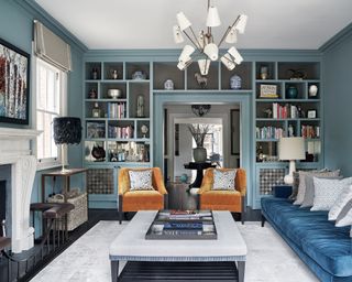 Small living room lighting with blue walls, blue sofa, orange armchairs and a sputnik chandlier with coned lampshades over the bulbs
