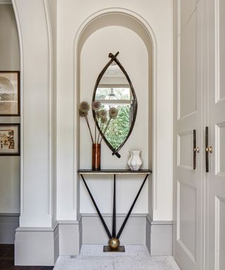 An entry table decor idea with minimal black table in an alcove with elliptical mirror